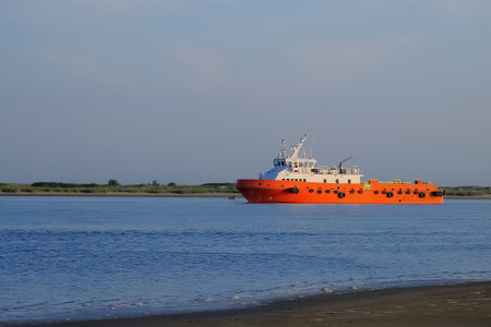 Orange vessel on calm blue water near grassy shoreline at sunset...の写真素材
