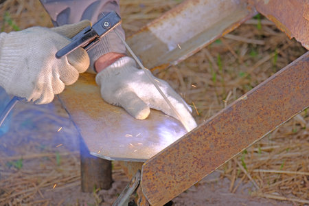 Close-up of manual metal welding with gloves and sparks flying outdoors.の写真素材