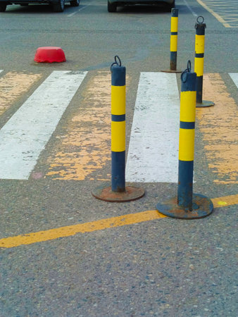 Rusty bollards with yellow stripes on a worn pedestrian crosswalk in a parking lot with asphalt background, concept of urban safety and decay..の写真素材