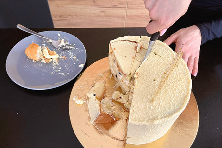 Female hands cut off a piece of festive cake with a knife