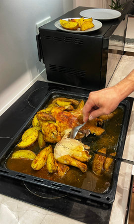 Hands cut baked chicken with potatoes with a knife.の写真素材