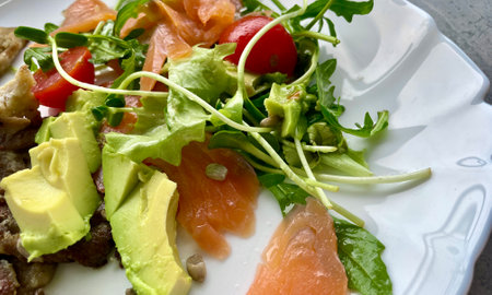 On a white plate - a salad of tomatoes, green arugula, avocado, salmon and mushroomsの写真素材