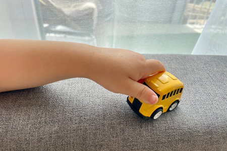 A childs hand is playing with a yellow small toy car