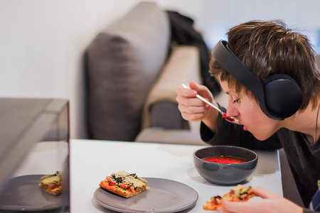 A teenager in headphones eats while listening to musicの写真素材