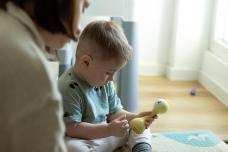 The child is sitting calmly playing with a toy, next to his motherの写真素材