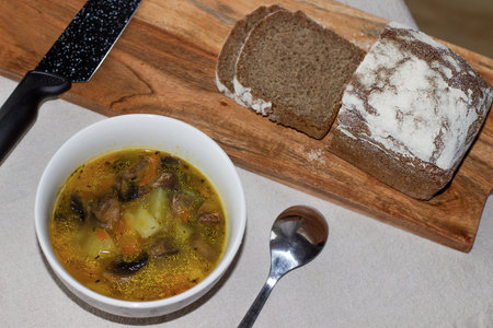 Mushroom soup in a white bowl, nearby on a wooden board are sliced pieces of rye breadの写真素材
