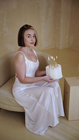Cute young woman with short hair and white dress holding birthday cake with candles for her birthdayの写真素材