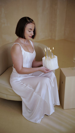 Cute young woman with short hair and white dress holding birthday cake with candles for her birthdayの写真素材