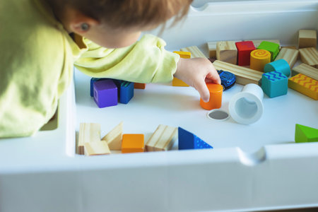 A small child plays with geometric wooden colored figures on a childrens tableの写真素材