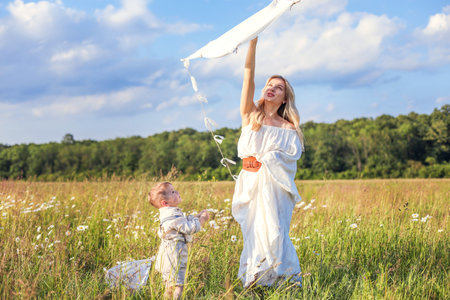 A little child and his mother are having fun in the meadow, flying a kiteの写真素材