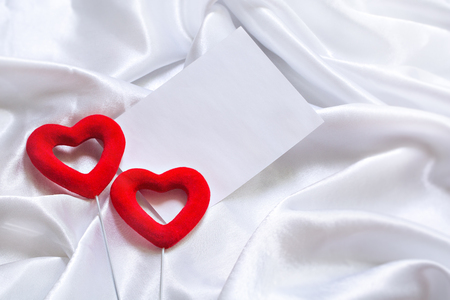The concept of two lovers hearts lying on the white satin with white sheet of paper for text can be used as a background, textureの写真素材