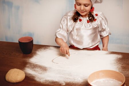 The little girl draws a finger heart on the scattered flour. Soft focusの写真素材