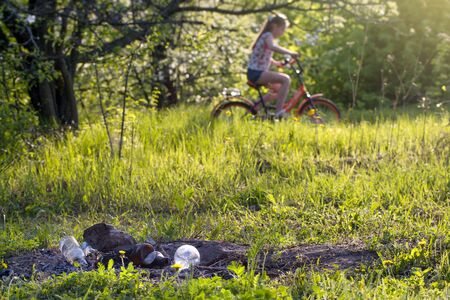 Burning garbage and air pollution. Plastic and glass bottles are recycled on green grass. Trash pollution in the nature.  Blurry people in the backgroundの写真素材