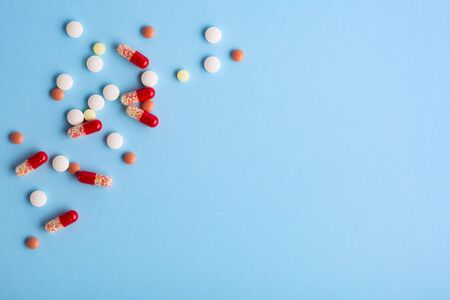 Heap of pills and capsules spilling  on blue background. Medicine concept. Copy space.の写真素材
