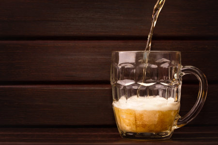 Beer pouring into a glass, with foam, on wooden table. Free copy space