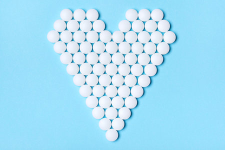 Heart made of white round pills on a blue background. Medical, pharmacy and healthcare concept. Top...