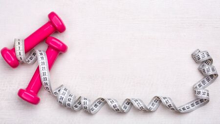 Creative flat lay overhead composition with 
pink female dumbbells and measuring tape on a light woodenの写真素材