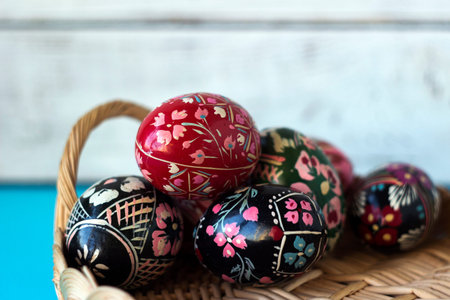 A lot of decorated Easter eggs lie in a basket, whte and blue background. Ukrainian Easter eggs with...