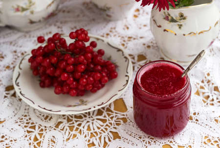 Healthy jam from viburnum berries (Viburnum opulus) in a glass jar, a bunch of viburnum, antique dishes and chrysanthemums in a vase. Preparations for the winter from coldsの写真素材