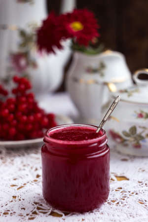 Healthy jam from viburnum berries (Viburnum opulus) in a glass jar, a bunch of viburnum, antique dishes and chrysanthemums in a vase. Preparations for the winter from coldsの写真素材