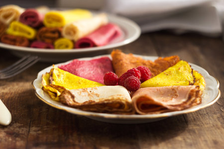 Multicolored flat pancakes on a plate decorated with raspberries. Original food pancakes on Maslyanitsaの写真素材