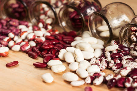 Multi-colored beans are poured out of jars on the table. White, red and colored beans. backgroundの写真素材