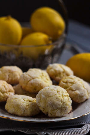 Round lemon cookies on a white plate surrounded by lemons fruit, gray wooden background. Homemade cookiesの写真素材