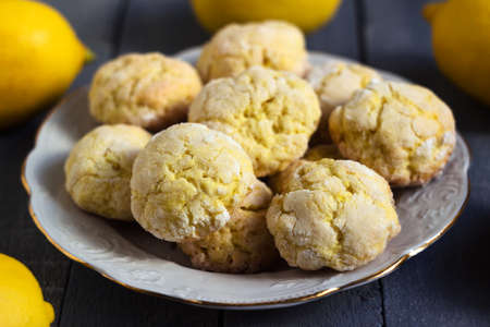 Round lemon cookies on a white plate surrounded by lemons fruit, gray wooden background. Homemade cookiesの写真素材