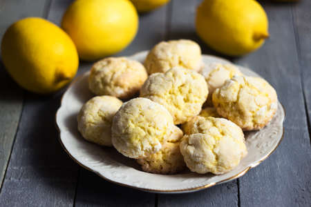 Round lemon cookies on a white plate surrounded by lemons fruit, gray wooden background. Homemade cookiesの写真素材