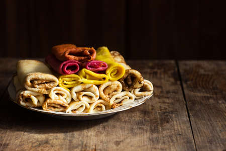 Multi-colored rolled pancakes on a white plate, wooden background. Morning food. pancake week. Place for textの写真素材
