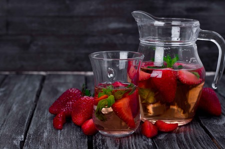 Strawberry lemonade with ice in glass and jar on wooden backgroundの写真素材