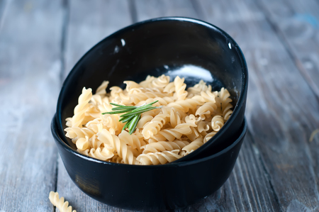 Raw pasta on wooden background and bowl of pastaの写真素材