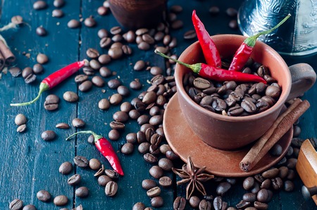 Coffee beans in a cup of chili, cinnamon and Dittany on a dark wooden background coffee beans scattered aroundの写真素材