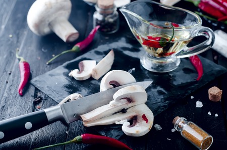 slices of mushrooms on a stone slate board and chili sauce in saucers on wooden dark backgroundの写真素材