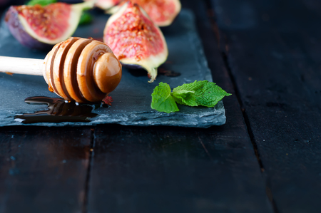 honey stick, Ripe purple figs and mint on dark slate board on wooden backgroundの写真素材