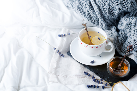 Warm knitted sweater,cup of hot tea with lavander on tray in bedの写真素材