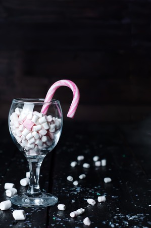 White, yellow and pink marshmallows with christmas candy in a large glass on the dark wooden backgroundの写真素材