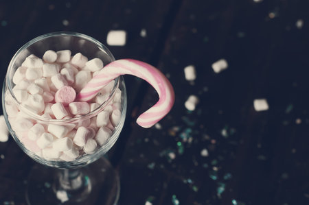 White, yellow and pink marshmallows with christmas candy in a large glass on the dark wooden backgroundの写真素材