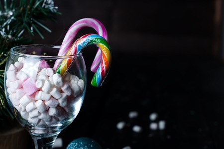 White, yellow and pink marshmallows with christmas candy in a large glass on the dark wooden backgroundの写真素材