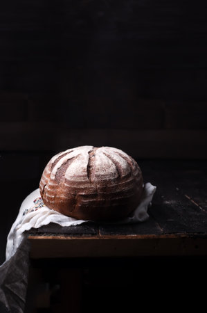 fresh crusty bread on old black embroidered table cloth on an old black wooden background