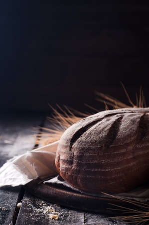 Rustic bread and wheat on dark wood table. Dark moody background with free text space.の写真素材