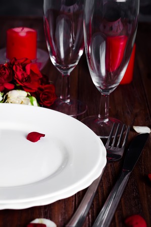 Romantic Valentine Candle Light Dinner Table Setting with red roses, gift and burning candles against a brown background.の写真素材