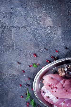 Raw juicy tenderloin with seasonings on a iron tray ready for roasting. Fresh pork meat steaks with Salsola and pepper shaker, colorful whole pepper, rock salt.の写真素材