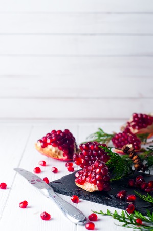Half pomegranate and pomegranate seeds and a branch of spruce on white wooden background. Copy spaceの写真素材