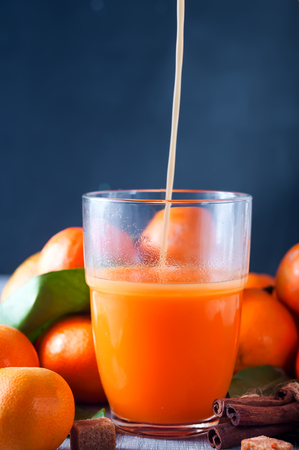 Healthy mandarin juice being poured into a glass, cinnamon sticks and tangerines on wooden tableの写真素材