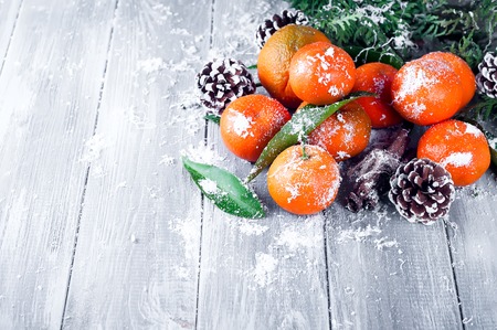 Composition with Tangerines Green Leaves, snow and Pine Cone Wooden Grey Backgroundの写真素材