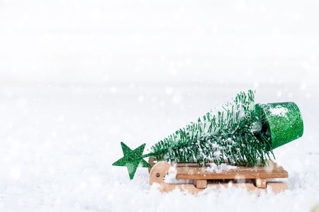 wooden winter sleigh carrying a small Christmas tree on a snow background