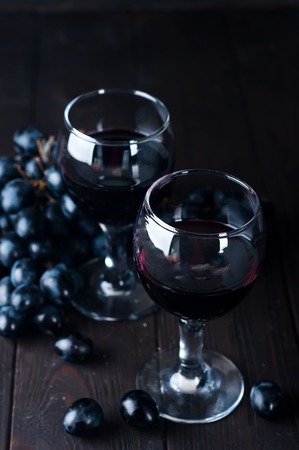 Red wine in glasses with dark grapes on a dark wooden backgroundの写真素材