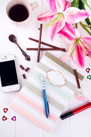 Cup of tea with chocolate, notebook, flowers, smartphone and cosmetics on the table. Still life of fashion woman, objects on whiteの写真素材