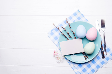Easter table setting with eggs, cutlery and napkin on a white wooden background with a piece of paper for your text on a plateの写真素材